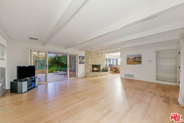 unfurnished living room featuring beamed ceiling, built in features, a stone fireplace, and light hardwood / wood-style flooring