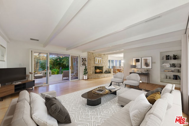 living room featuring built in shelves, beamed ceiling, a stone fireplace, and light hardwood / wood-style flooring