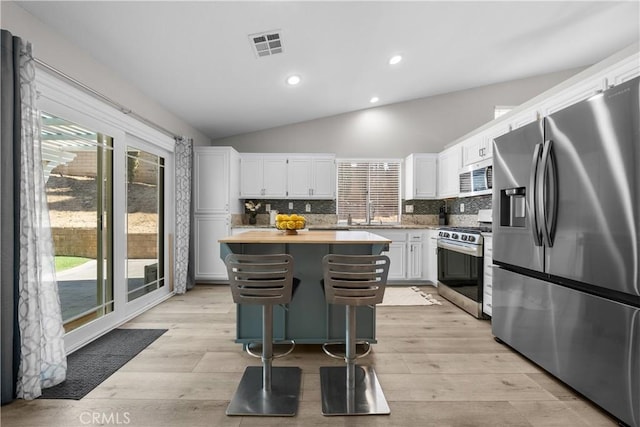 kitchen with lofted ceiling, a center island, decorative backsplash, white cabinetry, and appliances with stainless steel finishes