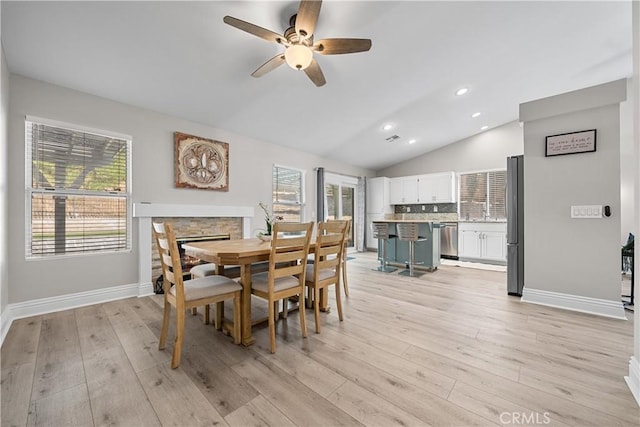 dining space with ceiling fan, light hardwood / wood-style flooring, a fireplace, and lofted ceiling