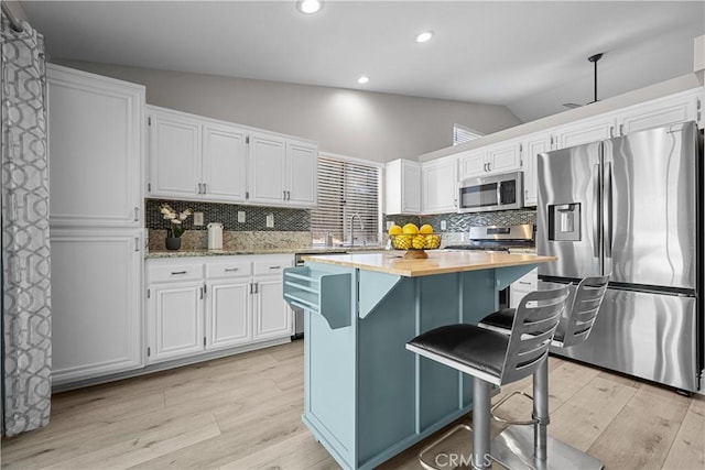 kitchen featuring vaulted ceiling, a center island, sink, appliances with stainless steel finishes, and white cabinets