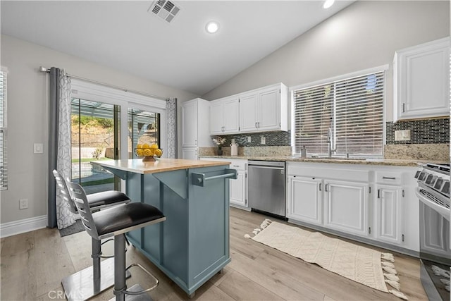 kitchen featuring appliances with stainless steel finishes, lofted ceiling, decorative backsplash, and white cabinetry