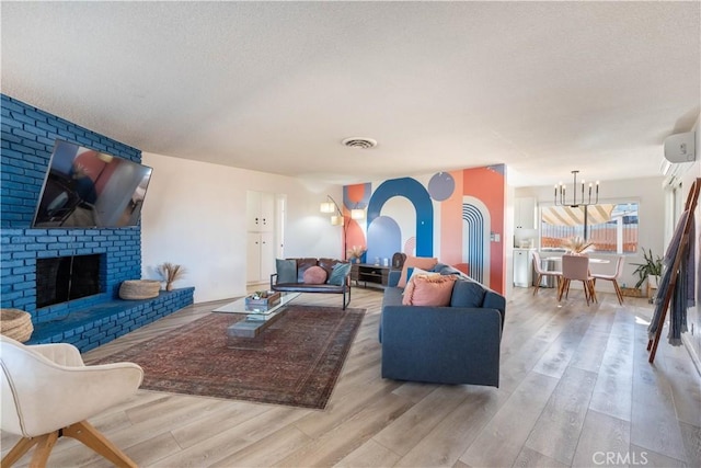 living room featuring light wood-type flooring, a textured ceiling, a fireplace, and a wall unit AC