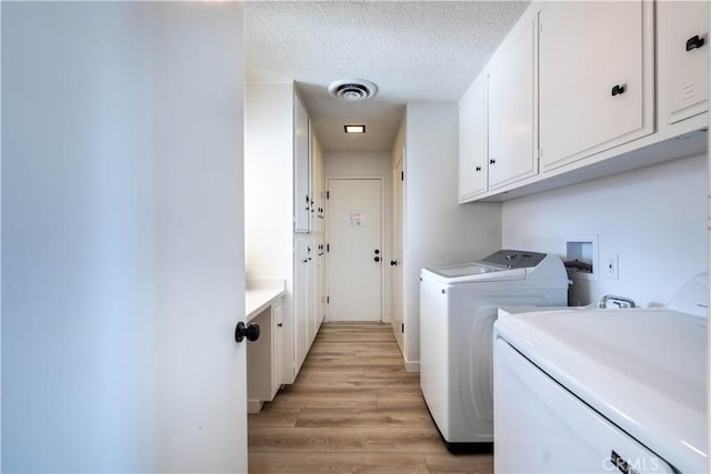 clothes washing area with light hardwood / wood-style floors, cabinets, a textured ceiling, and washing machine and clothes dryer