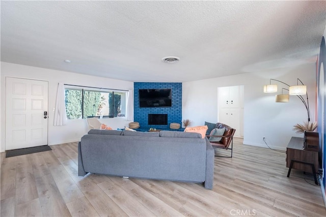 living room with light wood-type flooring, a brick fireplace, and a textured ceiling