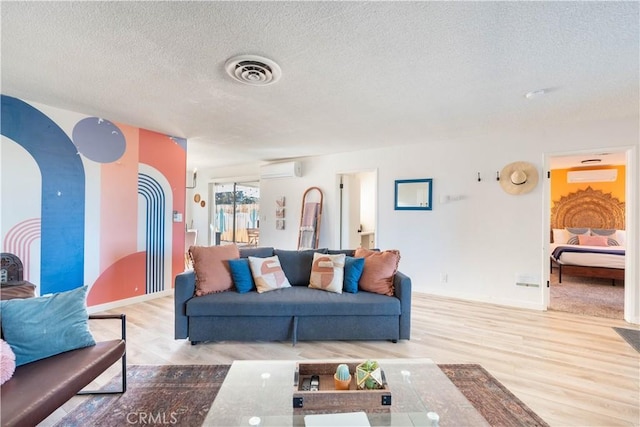 living room with a textured ceiling, light wood-type flooring, and a wall mounted air conditioner