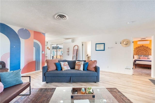 58387 Carlyle Dr, Yucca Valley, CA 92284 - living area with a textured ceiling, visible vents, a wall mounted air conditioner, wood finished floors, and baseboards