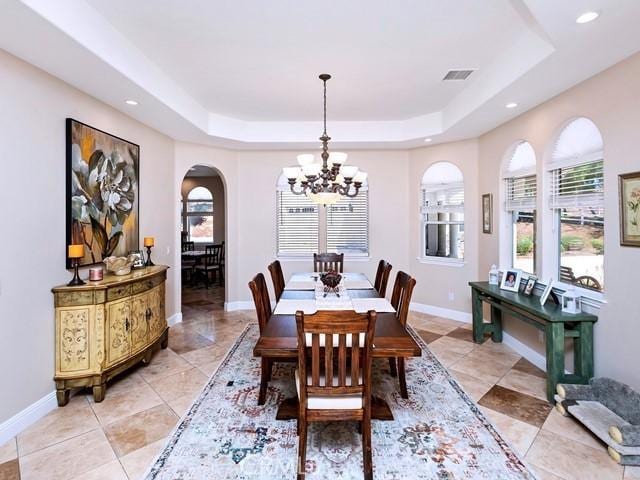 dining space with baseboards, visible vents, an inviting chandelier, arched walkways, and a raised ceiling