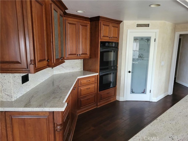 kitchen with dark wood-type flooring, double oven, backsplash, and light stone countertops