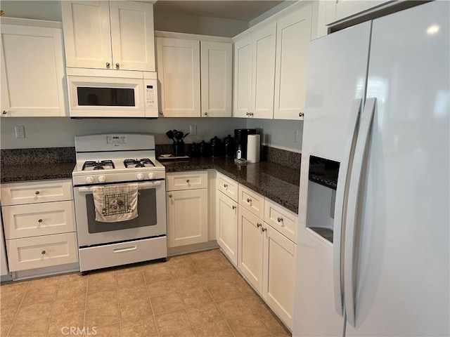 kitchen featuring dark stone counters, light tile patterned flooring, white appliances, and white cabinetry