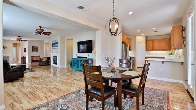 dining space featuring sink, ceiling fan with notable chandelier, and light hardwood / wood-style flooring