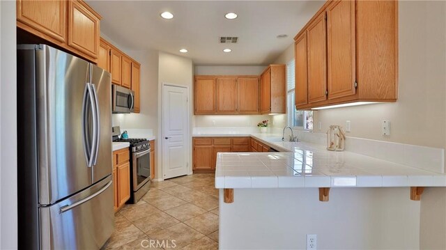 kitchen with kitchen peninsula, sink, appliances with stainless steel finishes, a kitchen breakfast bar, and tile counters