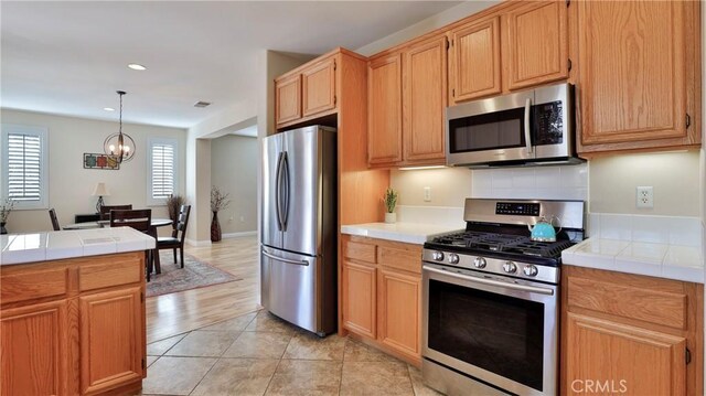 kitchen featuring tile counters, decorative light fixtures, stainless steel appliances, a chandelier, and light tile patterned flooring