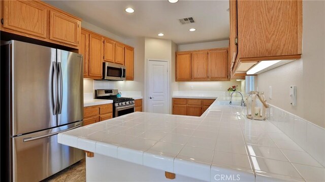 kitchen with appliances with stainless steel finishes, tile countertops, kitchen peninsula, and sink