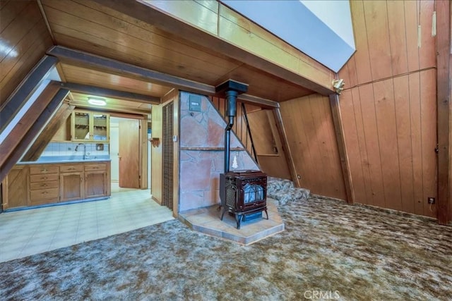 bonus room with wooden walls, light colored carpet, lofted ceiling, and a wood stove