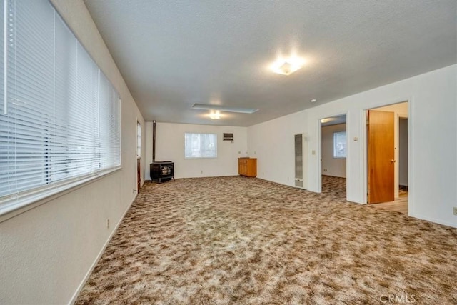 unfurnished living room with a wood stove, light colored carpet, and a textured ceiling