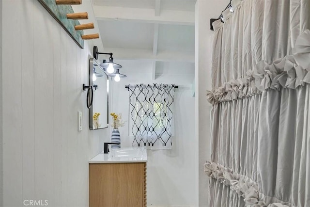 bathroom featuring wooden walls, beam ceiling, and vanity