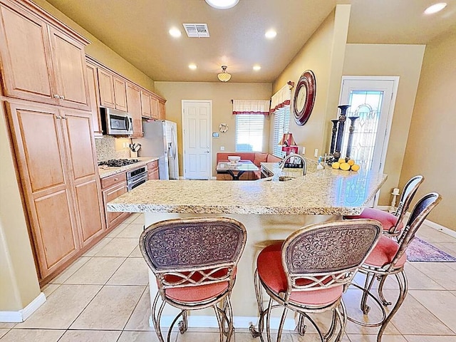 kitchen featuring decorative backsplash, a breakfast bar area, stainless steel appliances, light tile patterned floors, and light brown cabinetry