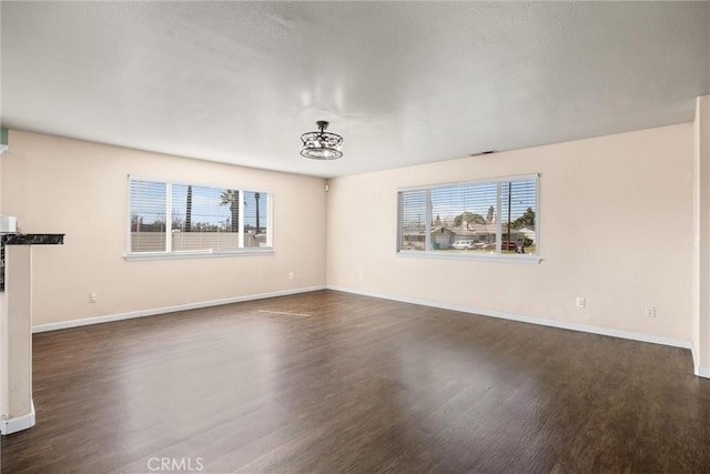 unfurnished room with baseboards, dark wood-style flooring, and a wealth of natural light