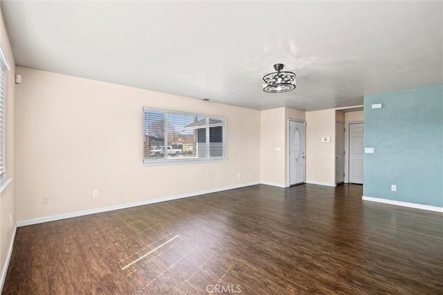 unfurnished room with a notable chandelier, dark wood-style flooring, and baseboards