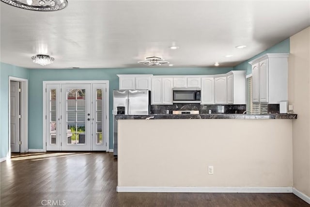 kitchen with a peninsula, appliances with stainless steel finishes, white cabinetry, and decorative backsplash