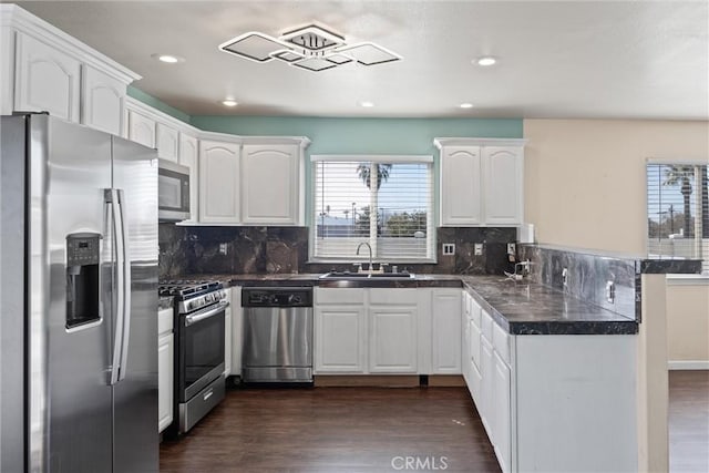 kitchen with dark wood-style floors, a peninsula, stainless steel appliances, white cabinetry, and a sink