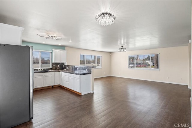 kitchen featuring dark countertops, open floor plan, freestanding refrigerator, a peninsula, and white cabinetry