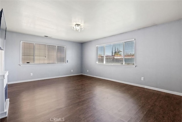 empty room featuring visible vents, baseboards, and dark wood finished floors