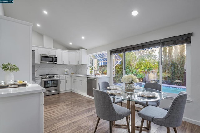 kitchen with white cabinetry, vaulted ceiling, light hardwood / wood-style floors, decorative backsplash, and appliances with stainless steel finishes