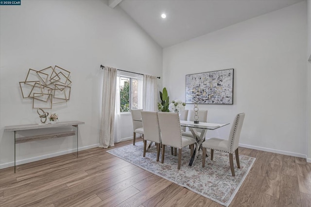 dining room featuring light wood-type flooring, high vaulted ceiling, and beamed ceiling