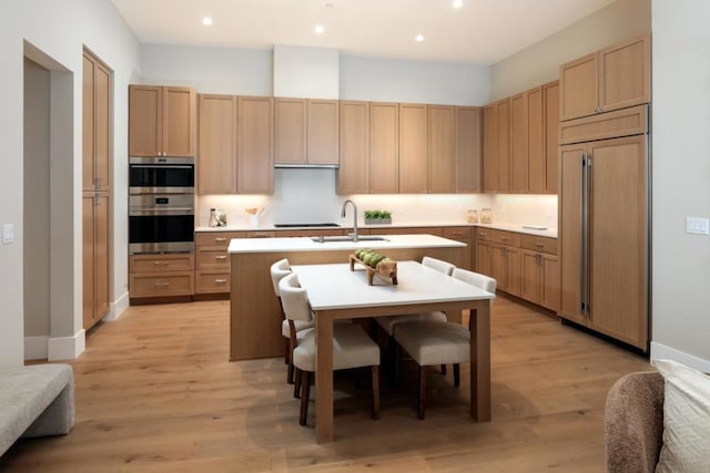 kitchen featuring double wall oven, light brown cabinetry, paneled built in fridge, light hardwood / wood-style flooring, and sink