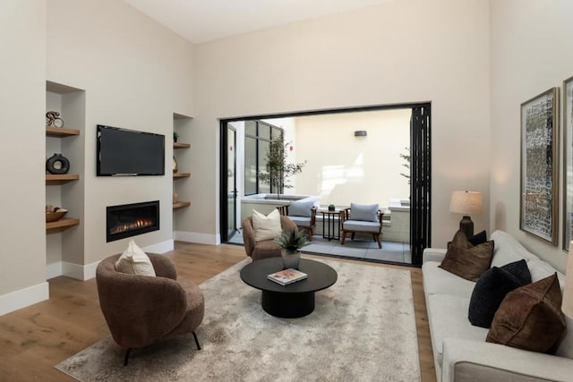 living room featuring built in shelves, light wood-type flooring, and a towering ceiling