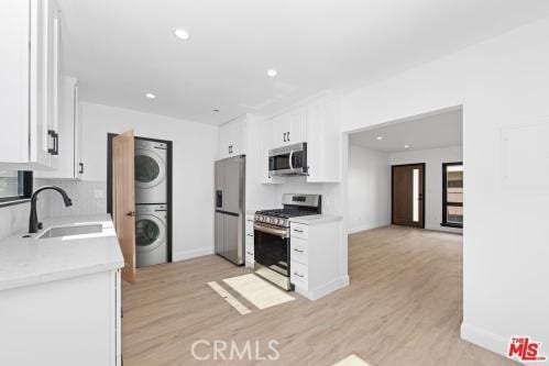 kitchen featuring stacked washer / dryer, white cabinetry, stainless steel appliances, sink, and light hardwood / wood-style flooring