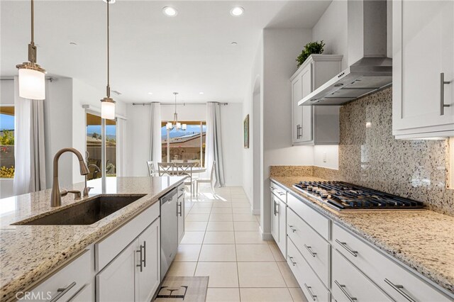 kitchen with decorative light fixtures, light stone countertops, sink, white cabinets, and wall chimney range hood