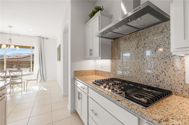 kitchen featuring white cabinetry, stainless steel gas stovetop, backsplash, light tile patterned floors, and wall chimney exhaust hood