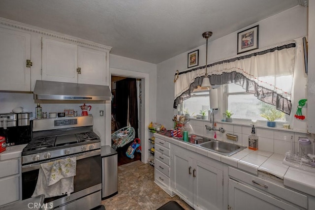 kitchen featuring under cabinet range hood, a sink, white cabinets, stainless steel gas range, and tile counters