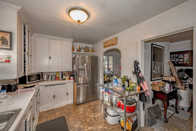 kitchen with arched walkways, stainless steel appliances, tile counters, and white cabinetry