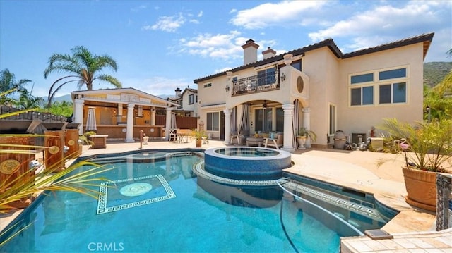 back of house with a balcony, a patio area, and a pool with hot tub