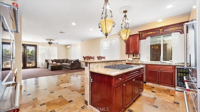 kitchen featuring ceiling fan, stainless steel gas cooktop, hanging light fixtures, light stone counters, and sink