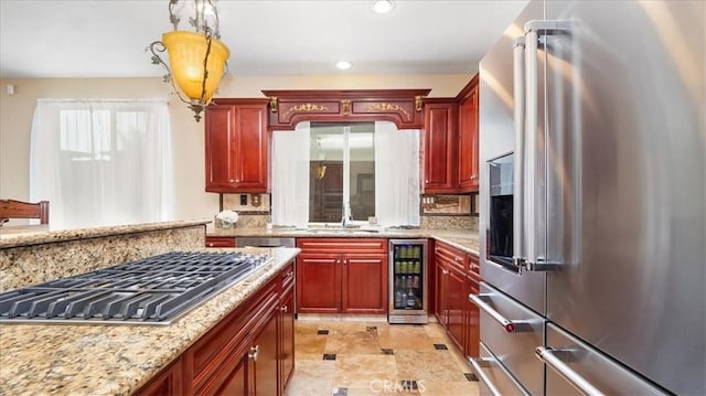 kitchen with appliances with stainless steel finishes, wine cooler, hanging light fixtures, light stone countertops, and sink