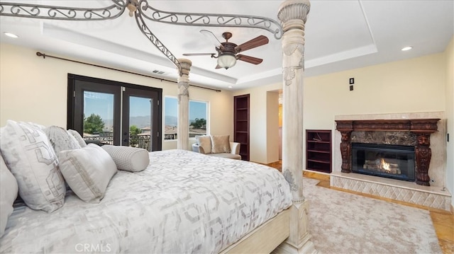 bedroom with ceiling fan, access to exterior, a raised ceiling, a premium fireplace, and french doors