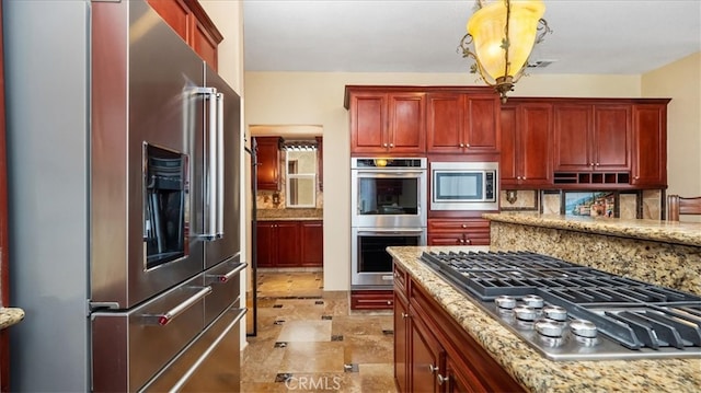 kitchen featuring appliances with stainless steel finishes, decorative backsplash, light stone counters, and decorative light fixtures