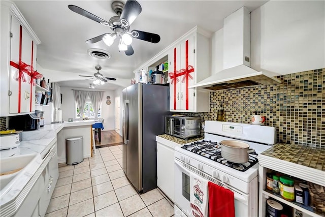 kitchen with white cabinets, wall chimney exhaust hood, backsplash, stainless steel fridge, and white gas range oven