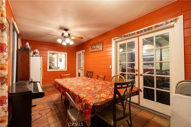 dining room with ceiling fan, french doors, and wood walls