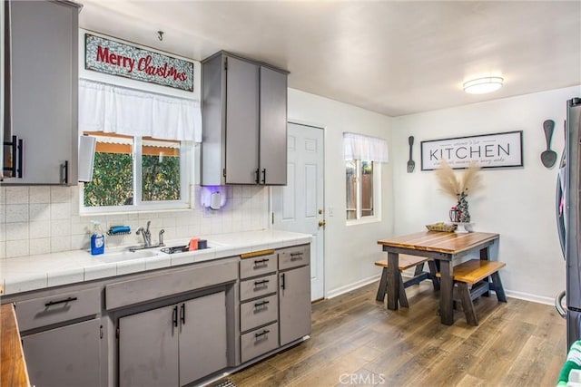 kitchen with sink, dark wood-type flooring, gray cabinetry, tile counters, and stainless steel fridge