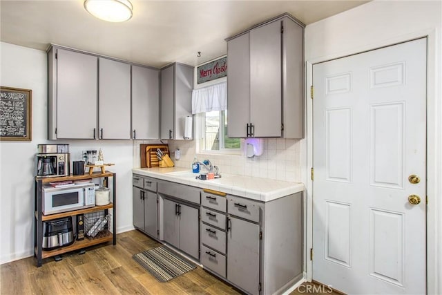 kitchen with tile countertops, gray cabinetry, wood-type flooring, and tasteful backsplash