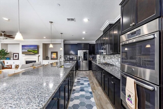 kitchen featuring sink, hanging light fixtures, tasteful backsplash, light stone counters, and stainless steel appliances