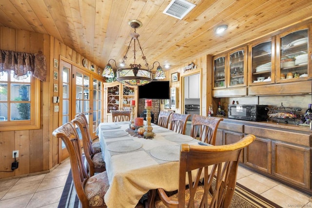 dining area featuring an inviting chandelier, light tile patterned floors, wood ceiling, and wooden walls