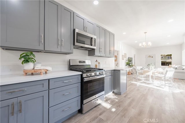 kitchen with appliances with stainless steel finishes, decorative light fixtures, light hardwood / wood-style flooring, and gray cabinetry