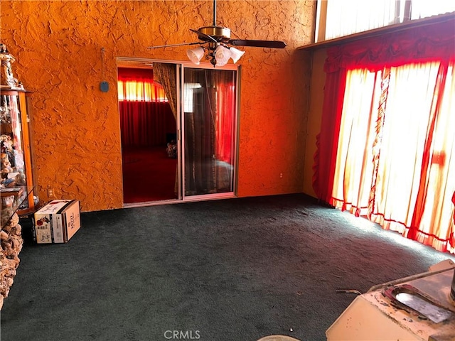 carpeted spare room featuring ceiling fan, a textured wall, and a healthy amount of sunlight